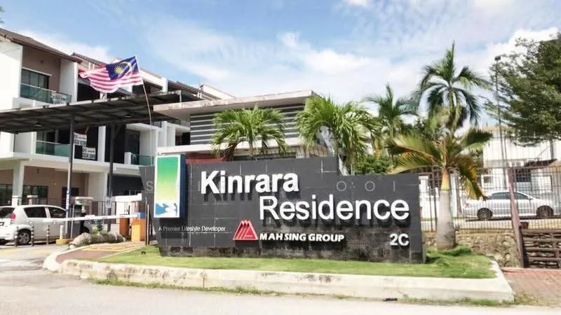 Exterior type: low-rise apartment block; features: signage with 'Kinrara Residence', landscaped entrance with palm trees, flagpole with Malaysian flag, modern architectural design, parking area visible, gated entry, surrounding greenery; style: modern.