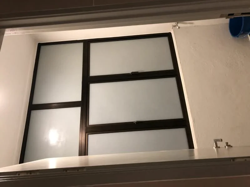 Room features: frosted glass windows, black window frames, white painted walls, ceiling light fixture, door frame, blue bucket.