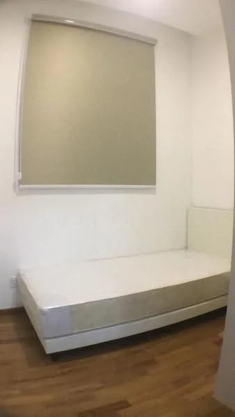 Bedroom features: single bed frame, wooden flooring, white painted walls, roller blinds, no bedding, corner wall with headboard, natural light from window, minimalist decor; style: minimalist.