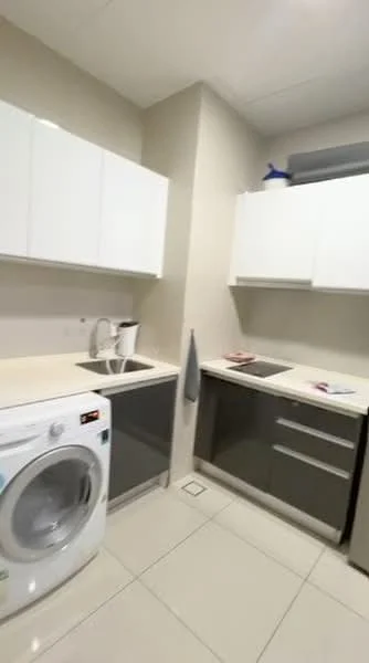 Kitchen features: white upper cabinets, grey lower cabinets, stainless-steel sink, chrome pull-down faucet, built-in stove, countertop with light-colored surface, washing machine, tile flooring, wall-mounted storage, kitchen towel hanging, minimalist design; style: modern.