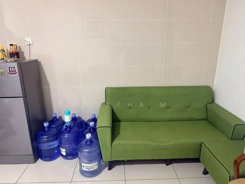 Living features: green fabric sofa, small side table, grey fridge, white tiled flooring, white tiled walls, 5 large water bottles.