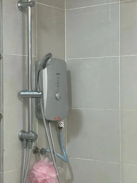 Bathroom features: shower head, water heater, chrome shower valve, grey tiled walls, grey tiled flooring, pink loofah, shower hose.