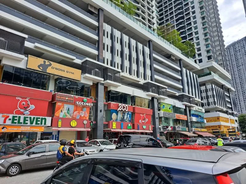 Exterior type: mixed-use development; features: multi-storey building, ground floor retail shops, 7-Eleven convenience store, Coconut shop, 2GO shop, Cross Gym signage, parking area in front, surrounding vehicles, urban setting, high-rise residential units above retail, glass facade, balconies on upper floors; style: modern.