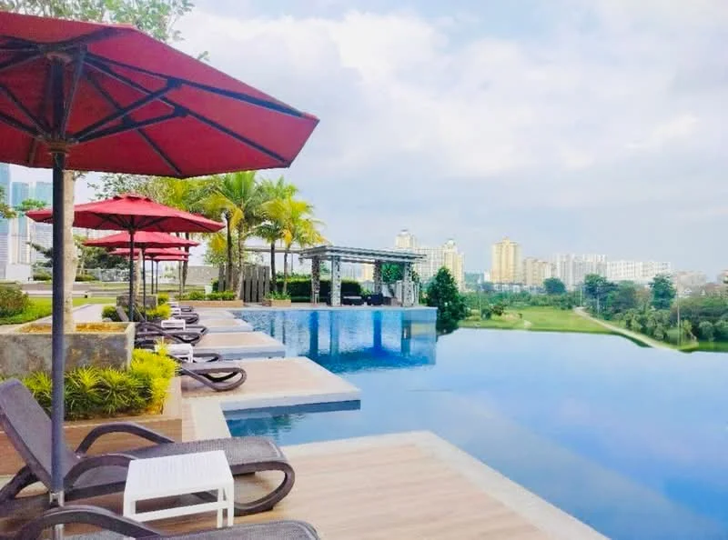 Exterior type: swimming pool deck; features: infinity pool, pool deck with loungers, red umbrellas, tropical landscaping, manicured lawn, view of city skyline, paved walkway, surrounded by greenery; style: modern.