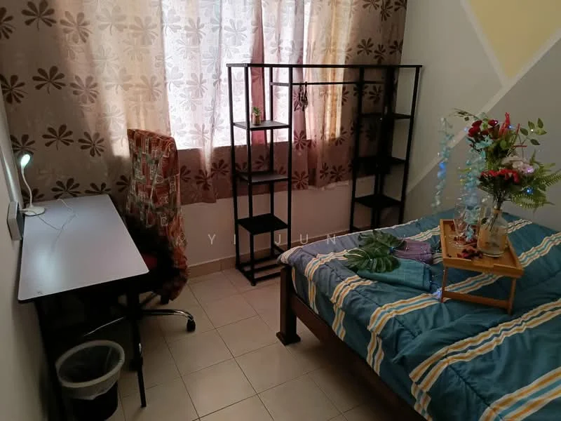 Bedroom features: queen-size bed with blue and yellow striped bedding, wooden bed frame, study desk with white surface, black metal shelving unit, decorative plant on tray, window with sheer curtains, tiled flooring, office chair with patterned upholstery, waste bin.