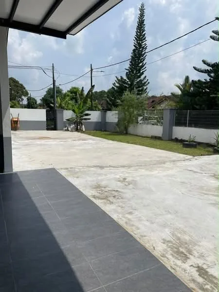 Exterior type: detached bungalow; features: concrete driveway, manicured lawn, mature trees, fenced perimeter, paved walkway, landscaped garden, single-storey structure, open space, visible utility poles, surrounded by greenery; style: modern.