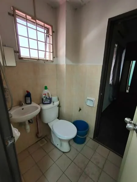 Bathroom features: white tiled walls, cream tiled flooring, one-piece toilet, sink with chrome faucet, mirror above sink, window with metal grille, blue plastic bin, cleaning supplies on sink, shower with handheld showerhead.