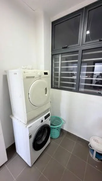 Laundry features: stacked front-load washing machine, front-load dryer, grey tiled flooring, white painted walls, window with horizontal grilles, plastic laundry basket, paint bucket.