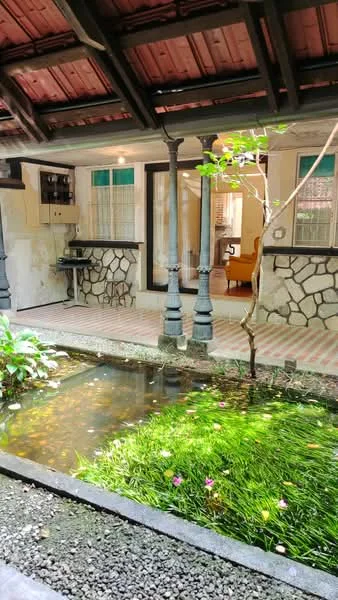 Room features: exposed wooden beams on ceiling, red tiled roof, stone wall cladding, brick flooring, decorative columns, indoor water feature with plants, green grass area, natural light from windows; style: traditional; view: garden.