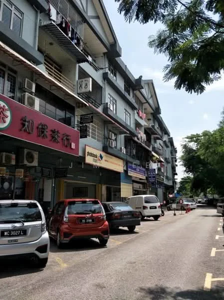 Exterior type: shophouse; features: 3-storey building, mixed-use commercial and residential, balconies on upper floors, air conditioning units visible, signage for various businesses, street parking available, trees lining the street, paved road, pedestrian walkway, multiple vehicles parked; style: modern.