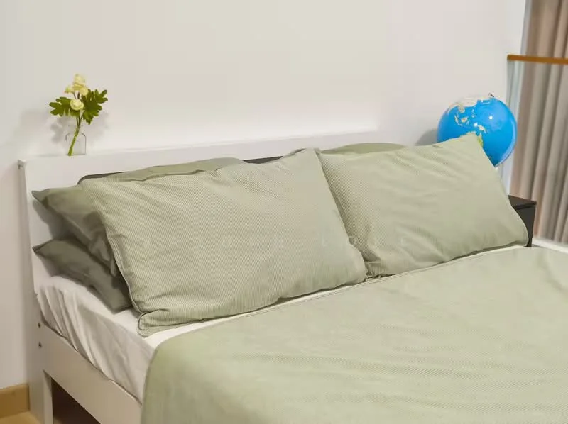 Bedroom features: queen-size bed, light green bedding, two green pillows, white bed frame, decorative flower on bedside, globe decoration, neutral wall color, wooden flooring; style: modern.