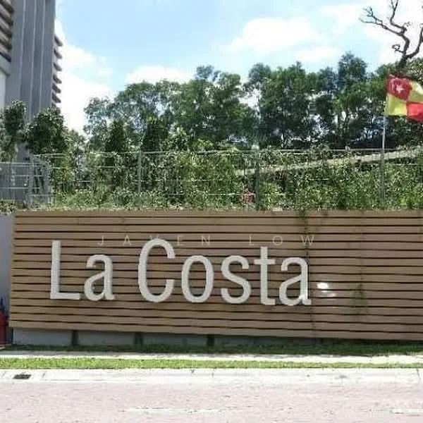Exterior features: wooden slat facade, landscaped greenery, signage with 'La Costa', flags displayed, paved walkway, surrounding trees; style: modern.
