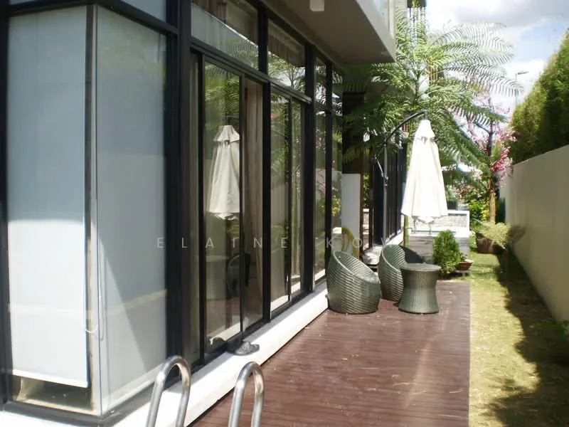 Exterior type: detached bungalow; features: large glass windows, wooden deck flooring, outdoor seating area with wicker chairs, umbrella for shade, manicured lawn, tropical landscaping with palm trees, fenced garden area; style: modern.