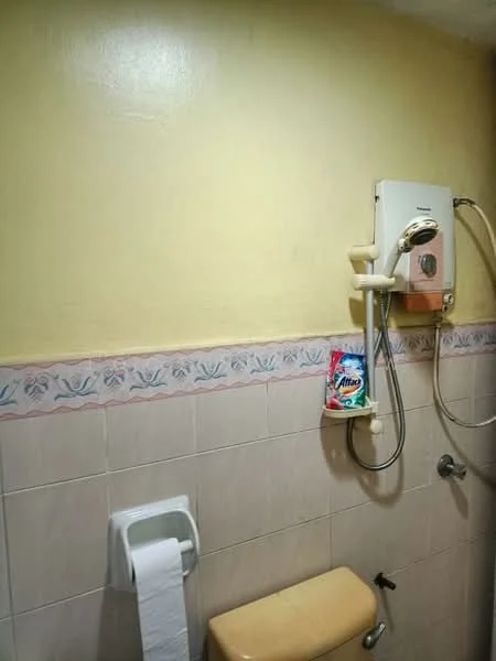 Bathroom features: yellow painted walls, white tiled walls, shower head with hose, toilet, toilet paper holder, decorative border tile, light fixture, water heater.
