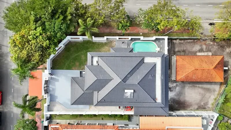 Exterior type: detached bungalow; features: flat roof, grey tiled roof, swimming pool, manicured lawn, paved walkway, surrounded by mature trees, driveway, fenced perimeter, adjacent to main road; style: modern.