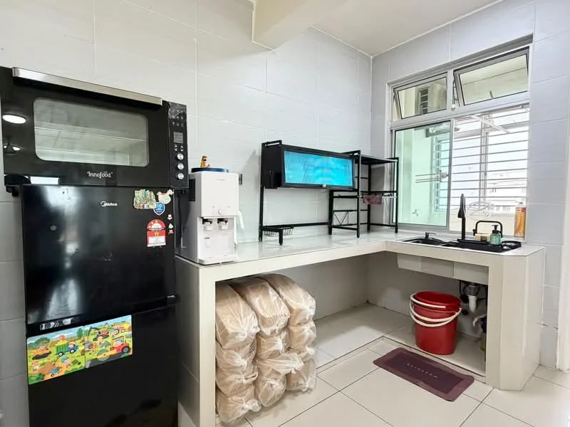 Kitchen features: black fridge, built-in oven, water dispenser, L-shaped countertop, white tiled walls, white tiled flooring, window with blinds, sink with faucet, storage shelves, red trash bin, stacked bags, kitchen mat; style: modern.