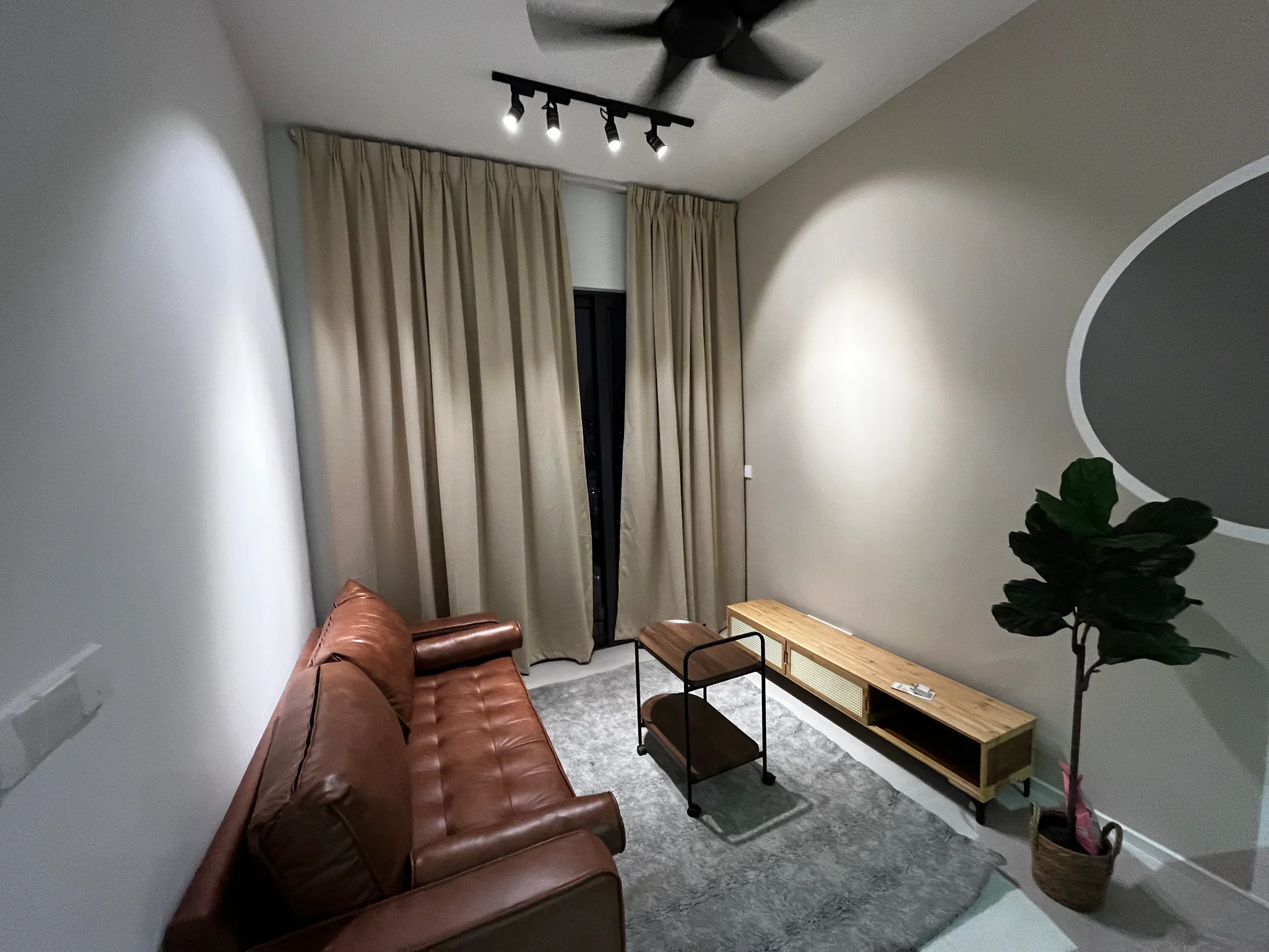 Living features: 3-seater leather sofa in brown, wooden coffee table, TV console with storage, area rug in grey, floor-to-ceiling curtains in beige, ceiling fan with light, wall-mounted light fixtures, decorative plant in pot; style: modern.