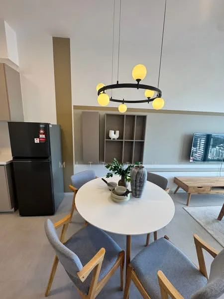 Dining features: round dining table, 4 upholstered dining chairs with wooden legs, pendant light fixture with yellow bulbs, grey cabinetry, black refrigerator, wall-mounted TV, light-colored flooring, decorative vase on table, shelf unit with decorative items; style: modern.