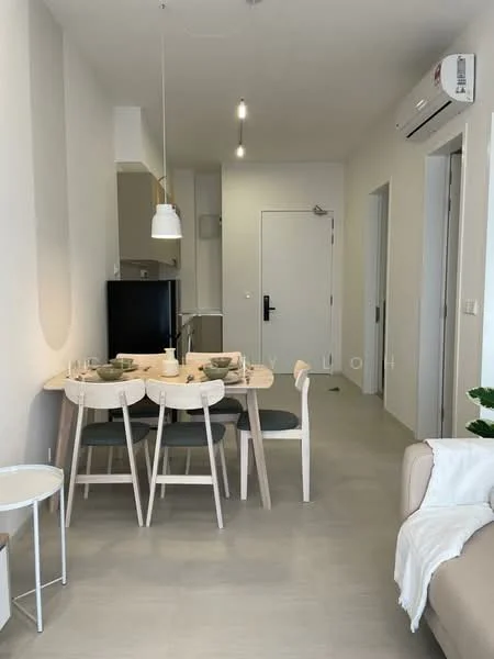 Dining features: round dining table, 4 dining chairs, white pendant lamp, light grey walls, light grey flooring, built-in kitchen cabinetry, black fridge, wall-mounted air conditioning unit, open layout, doorway to hallway, decorative plant; style: modern. Living features: beige fabric sofa, white throw blanket, small side table; style: modern.