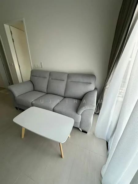 Living features: 3-seater fabric sofa in grey, white coffee table with wooden legs, floor-to-ceiling windows, sheer curtains, light-colored walls, light-colored flooring, decorative wall with no visible artwork, natural light from window; style: modern.