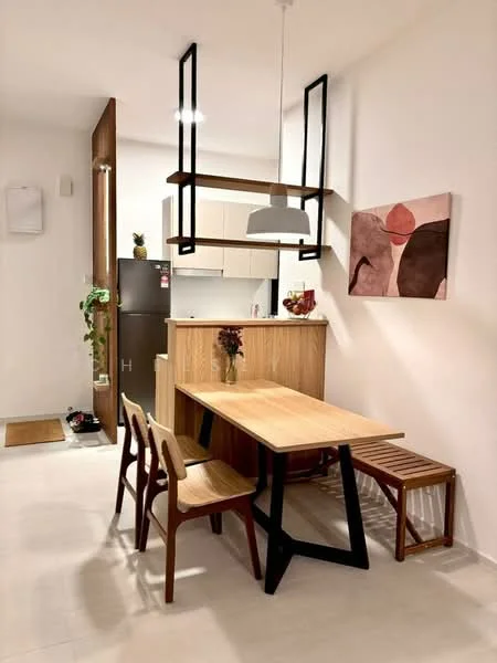 Dining features: wood dining table with black legs, 4 wooden dining chairs, pendant light fixture, wall-mounted shelf, framed artwork on wall, refrigerator, wood cabinetry, white walls, light-colored flooring, greenery in corner; style: modern. Kitchen features: white cabinetry, countertop, open layout to dining area; style: modern.