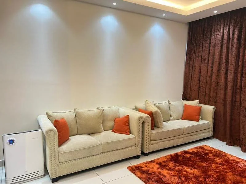 Living features: 2 beige fabric sofas with orange cushions, orange area rug, cream painted walls, recessed downlights, brown curtains, air purifier, tile flooring; style: modern.
