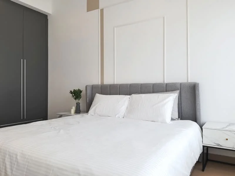 Bedroom features: king-size bed with upholstered headboard, white striped bedding, grey bedside table, marble-top bedside table, built-in wardrobe with grey doors, decorative plant on bedside table, white painted walls, soft lighting; style: modern.