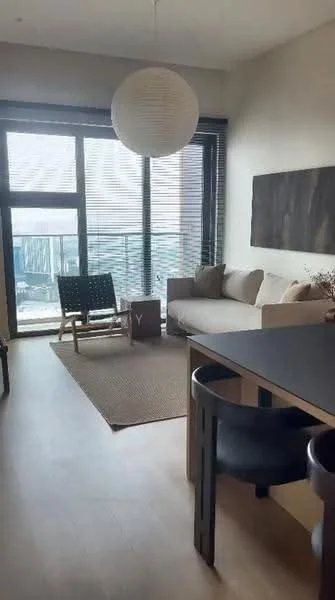 Living features: light wood flooring, floor-to-ceiling windows, roller blinds, beige fabric sofa, black dining table, black dining chairs, area rug with neutral color, decorative wall art, hanging pendant light; style: modern; view: city.