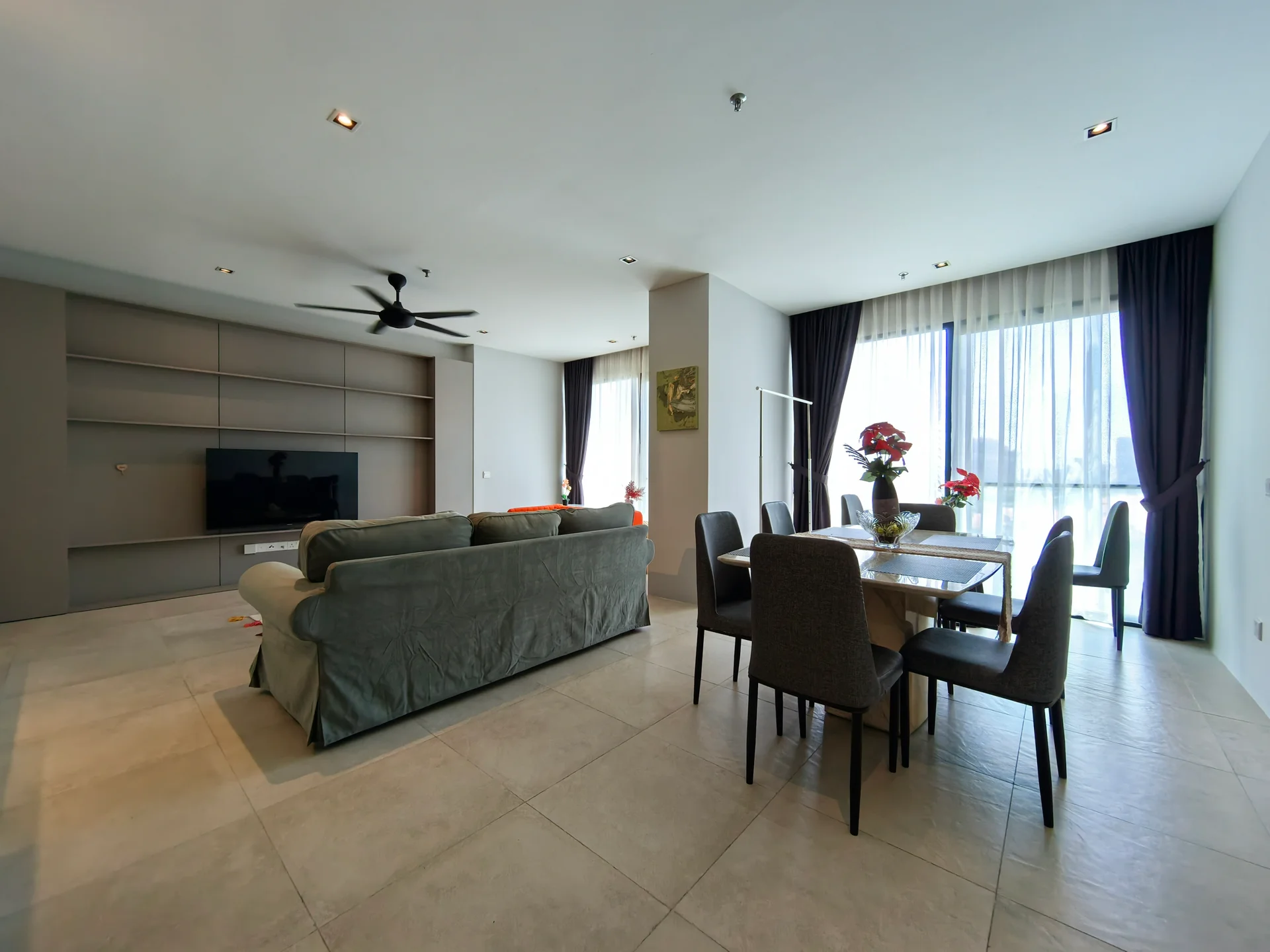 Living features: 3-seater fabric sofa in grey, coffee table, wall-mounted TV, TV console, dining table for 6, upholstered dining chairs, ceiling fan, floor-to-ceiling windows, sheer curtains, tile flooring, decorative plants, built-in shelving unit; style: modern; view: city.