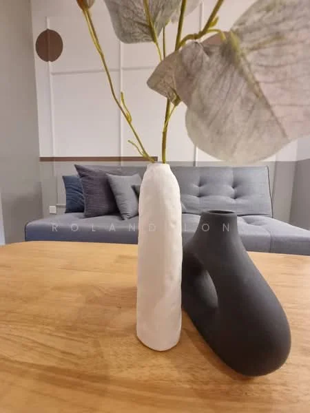 Room features: wooden dining table, white ceramic vase, black decorative vase, greenery in vase, grey sofa in background, cushions on sofa, neutral wall color, minimalist decor; style: modern.