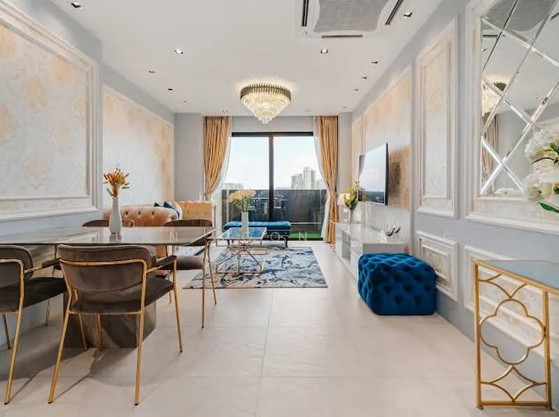 Living features: chandelier, recessed downlights, floor-to-ceiling windows, sliding glass door, cream wallpaper with floral pattern, blue accent chair, beige sofa, glass coffee table, decorative area rug, gold-framed side table, blue ottoman, dining table with chairs, curtains, wall-mounted TV, decorative vases; style: luxury; view: city.