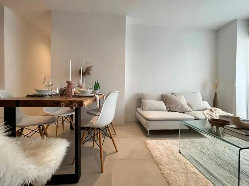 Living features: light grey walls, large windows with natural light, sofa in light grey fabric, glass coffee table, area rug in cream, wood dining table with black metal legs, white dining chairs with wooden legs, decorative vase with dried plants, candles on the dining table, tableware including glasses and plates; style: modern.
