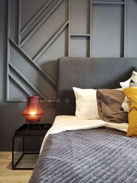 Bedroom features: grey upholstered headboard, decorative wall paneling with geometric design, plaid patterned bedding, decorative throw pillows in various colors, black bedside table, table lamp with a red shade, wooden flooring, neutral wall color; style: modern.