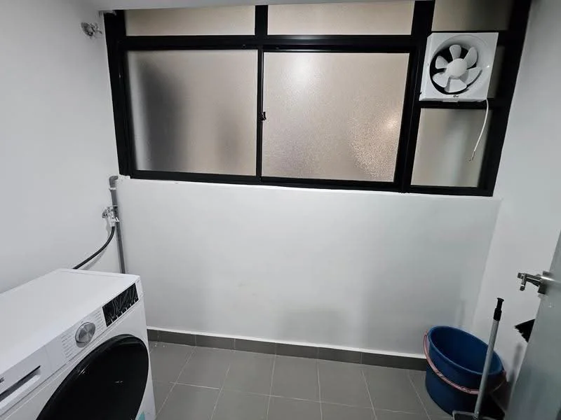 Laundry features: front-load washing machine, grey tiled flooring, white painted walls, black-framed window, frosted glass window, wall-mounted exhaust fan, plastic laundry basket.