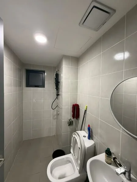 Bathroom features: grey tiled walls, white tiled flooring, round mirror, single-sink vanity, chrome basin mixer, one-piece toilet, shower area with wall-mounted showerhead, window for natural light, recessed ceiling lights, towel rack, cleaning supplies, waste bin; style: modern.