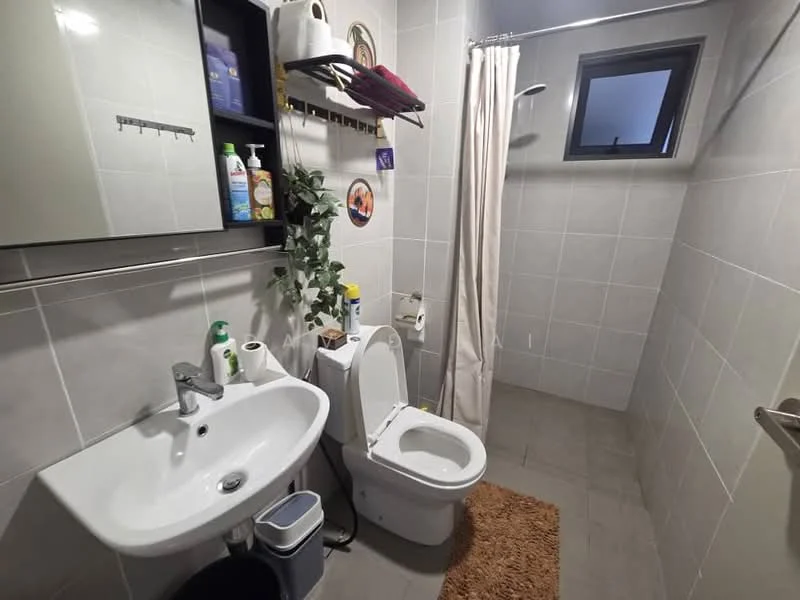 Bathroom features: white ceramic toilet, single-sink vanity with chrome faucet, mirror above sink, shower area with glass partition, grey tiled walls, light grey floor tiles, shower curtain, plant decor, toilet paper holder, soap dispenser, cleaning supplies on shelf; style: modern.