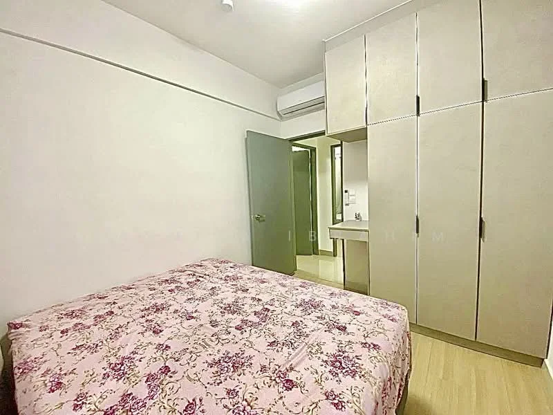 Bedroom features: queen-size bed with floral bedding, built-in wardrobe with sliding doors, light wood flooring, white painted walls, air conditioning unit, window with no visible treatment, small desk area visible, door leading to bathroom, ceiling light fixture; style: modern.