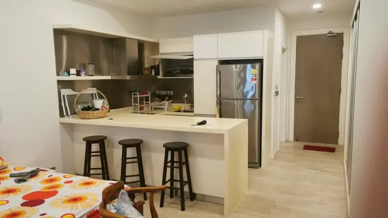 Kitchen features: white cabinetry, stainless-steel refrigerator, stainless-steel sink, chrome faucet, countertop with bar seating, three wooden bar stools, open shelving, tile backsplash, built-in oven, microwave, ceramic tile flooring, light-colored walls, recessed lighting; style: modern. Room features: dining table with floral tablecloth, wooden chair, entrance door.