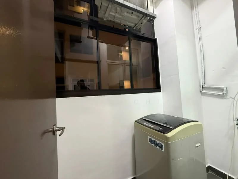 Laundry features: washing machine, window with black frame, white painted walls, grey tiled flooring, door, exposed pipes.