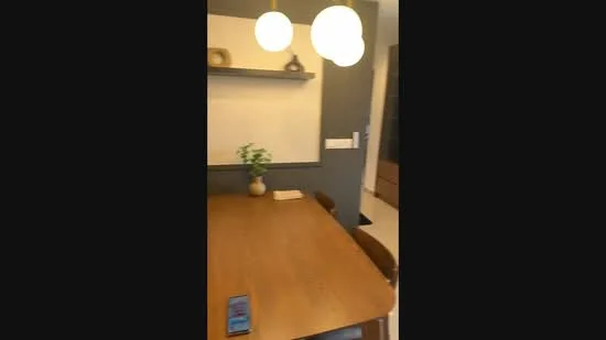 Dining features: wood dining table, upholstered dining chairs, pendant lighting, decorative wall shelf, greenery in vase, neutral wall color, dark accent wall, flooring with light tiles; style: modern.