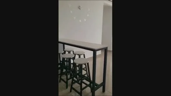Room features: bar counter with white marble top, black metal frame, 4 high stools with white seats, white painted walls, clock on wall, tile flooring; style: modern.