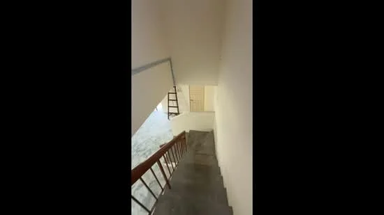Room features: staircase with wooden railing, grey tiled flooring, white painted walls, natural light from upper level, open space, no visible decor; style: minimalist.