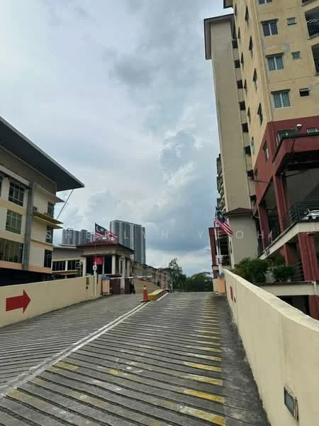 Exterior type: multi-storey car park; features: sloped driveway, concrete surface, guard house at entrance, visible parking spaces, surrounded by buildings, city skyline in background, flag poles with flags, clear sky with clouds; style: modern.