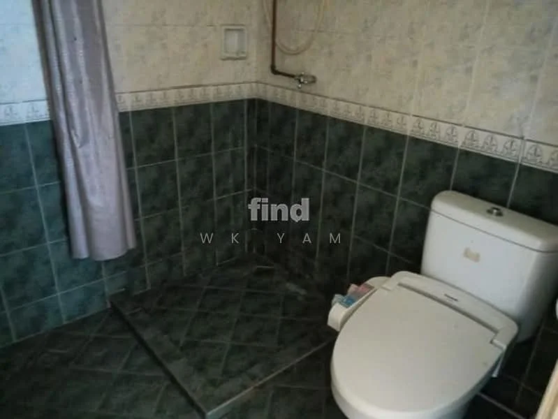 Bathroom features: white one-piece toilet, shower with handheld showerhead, green tiled walls, grey tiled flooring, curtain for shower area, wall-mounted soap holder, decorative border tile, corner shower area.
