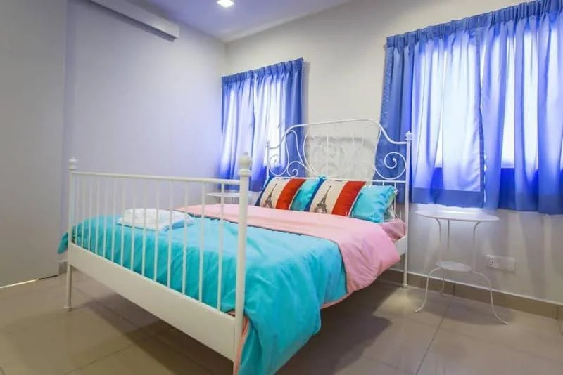 Bedroom features: white metal bed frame, queen-size bed, light blue bedding, pink throw blanket, decorative pillows in various colors, white bedside table, two blue curtains, tile flooring, recessed ceiling lights, wall-mounted light switch; style: modern.
