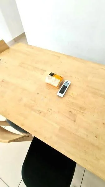 Dining features: wooden dining table, black dining chair, remote control on table, packaged item on table, light-colored flooring, white painted walls; style: modern.