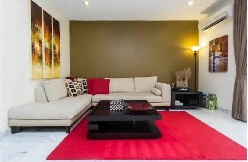 Living features: L-shape sectional sofa in beige, decorative cushions in red and black, coffee table with black finish, area rug in red, marble flooring, feature wall in olive green, wall-mounted air conditioning unit, floor lamp, framed artwork on wall, curtains in neutral color; style: modern.