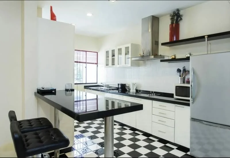 Kitchen features: black granite countertop, white cabinetry with flat-panel doors, stainless-steel refrigerator, built-in oven, four-burner gas hob, stainless-steel range hood, black and white checkered tile flooring, single-bowl stainless-steel sink, window with red blinds, microwave, open shelving, bar counter with two black stools; style: modern.