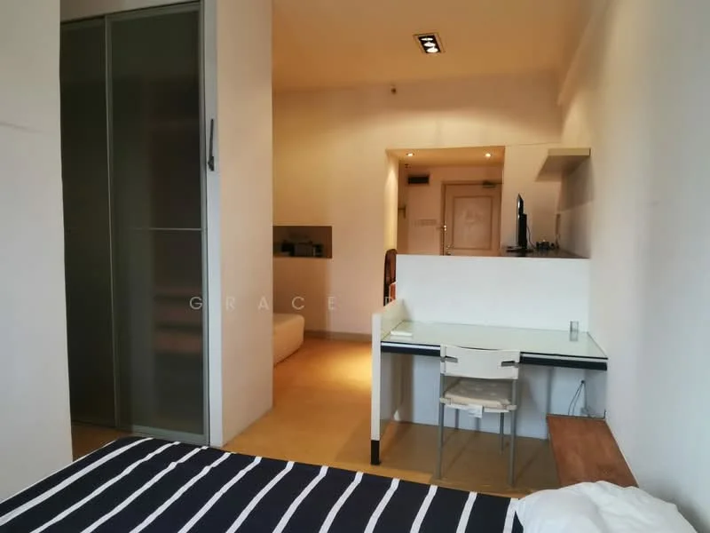 Room features: white painted walls, wooden flooring, desk with glass top, white chair, built-in wardrobe with sliding doors, wall-mounted TV, recessed ceiling lights, open kitchen area visible in background; style: modern.