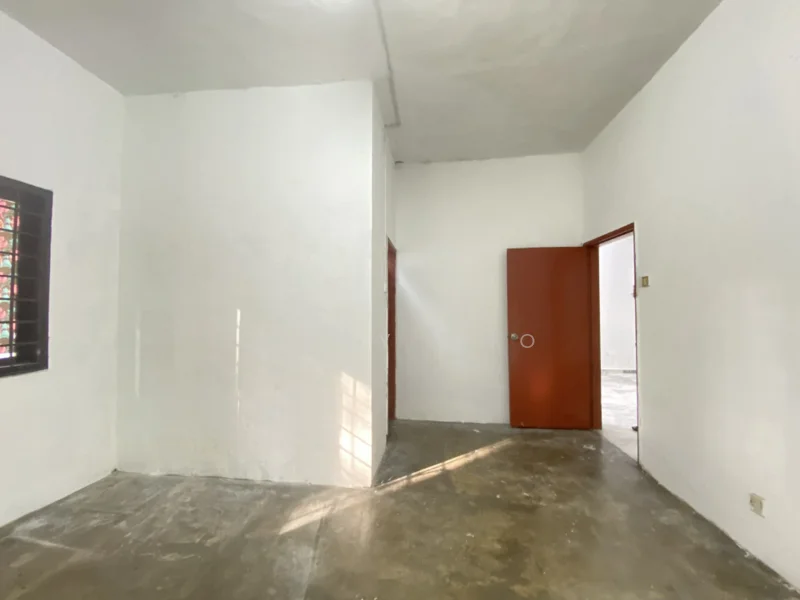 Room features: white painted walls, concrete flooring, two red doors, window with wooden grille, natural light from window.